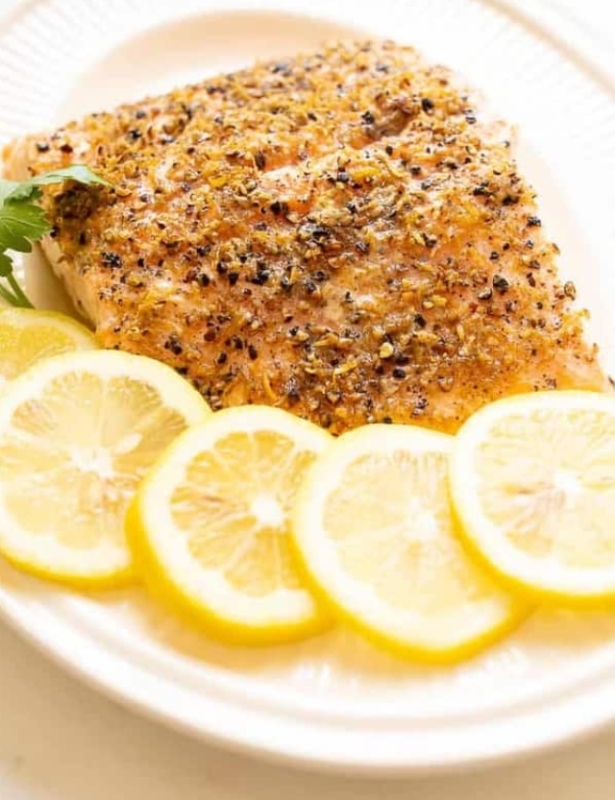 Baked lemon pepper salmon on a white oval dish garnished with sliced lemon and parsley