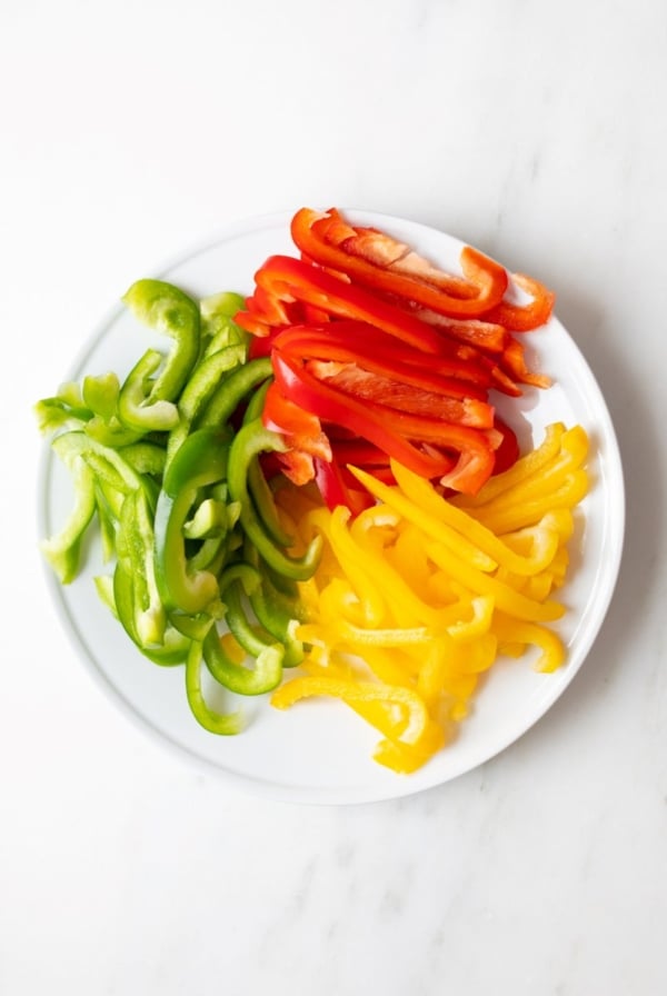 Fresh sliced colorful bell peppers on a white plate, resting on a marble countertop.