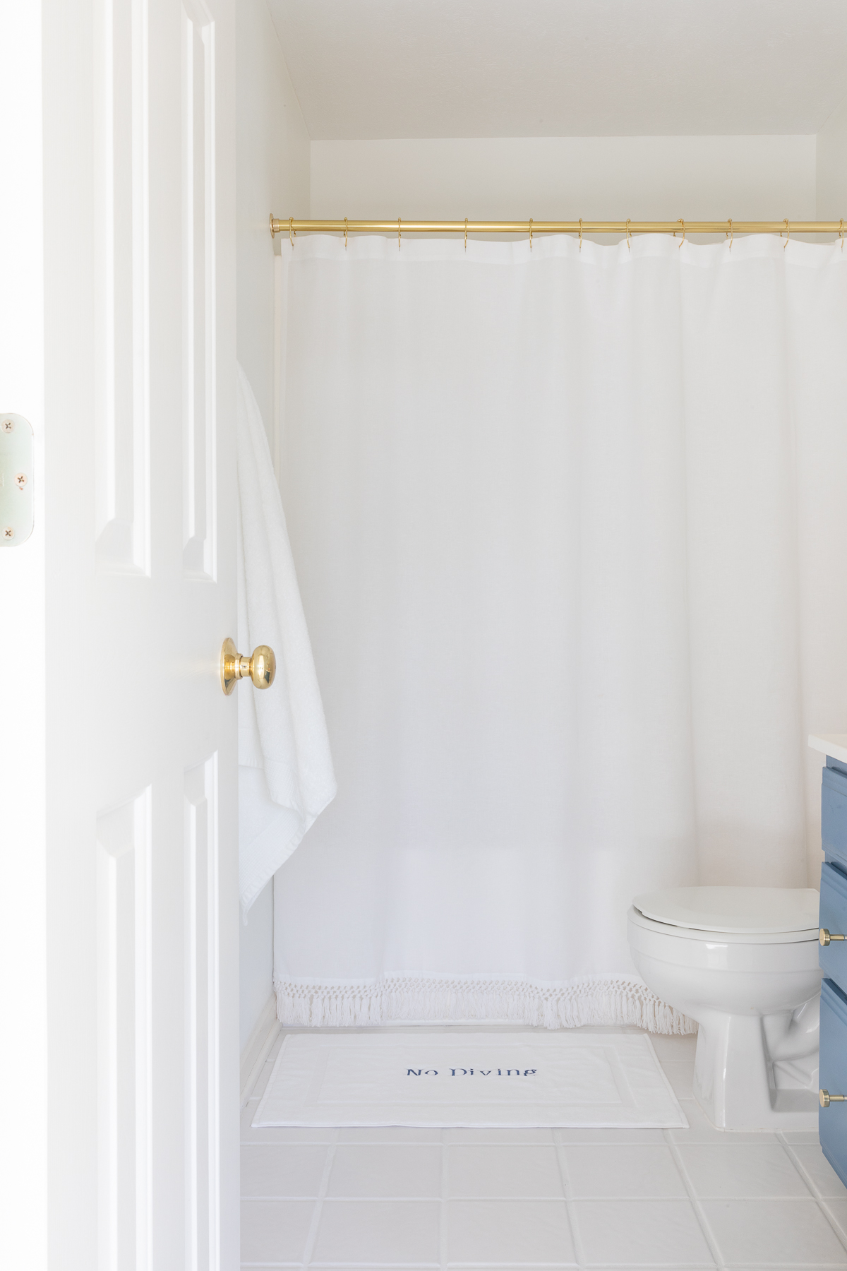 brass and white lake house bathroom with tassel shower curtain and no diving bath mat