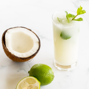 A coconut mojito recipe with a sliced coconut and limes next to it.