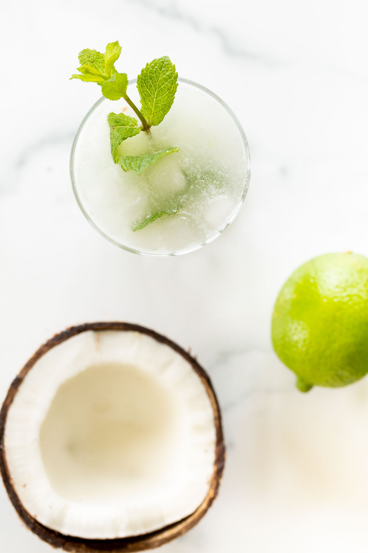 A coconut mojito recipe with a sliced coconut and limes next to it. 