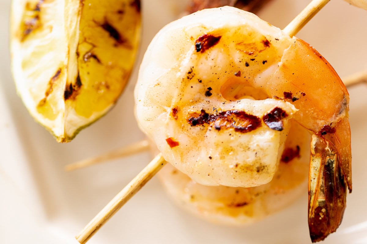 Close-up of tequila lime shrimp skewers with char marks, accompanied by a grilled lemon wedge.