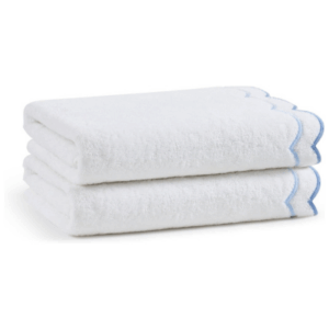 Two folded white towels with blue scalloped edges, stacked neatly against a plain background—perfect for adding a fresh, welcoming touch to any guest room.