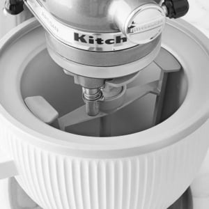 Black and white image of kitchen gadgets, including a KitchenAid stand mixer with a whisk attachment and mixing bowl.
