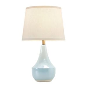 A ceramic table lamp with a glossy white and light blue base and a beige fabric lampshade, perfect for brightening up your guest room, pictured against a plain white background.