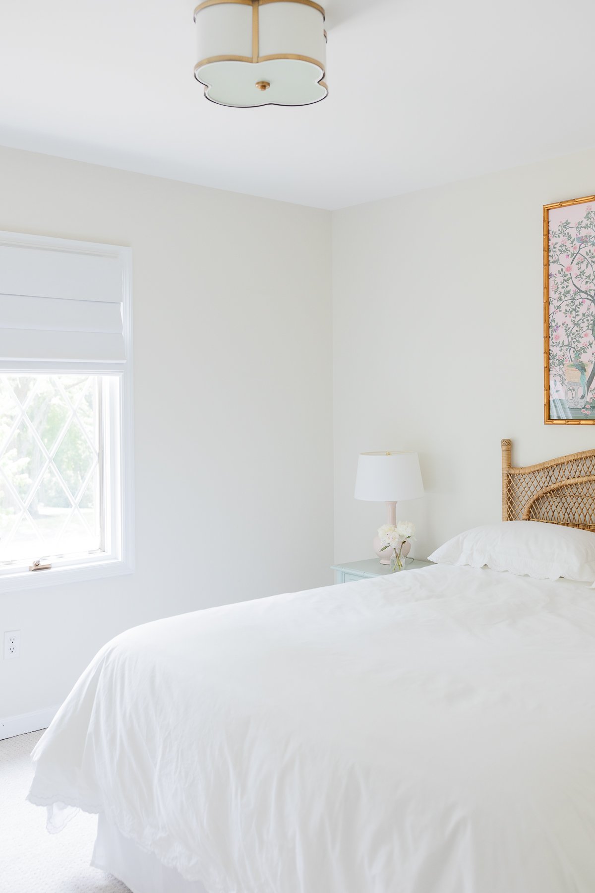 A guest bedroom with a rattan headboard and pink and green chinoiserie art above.