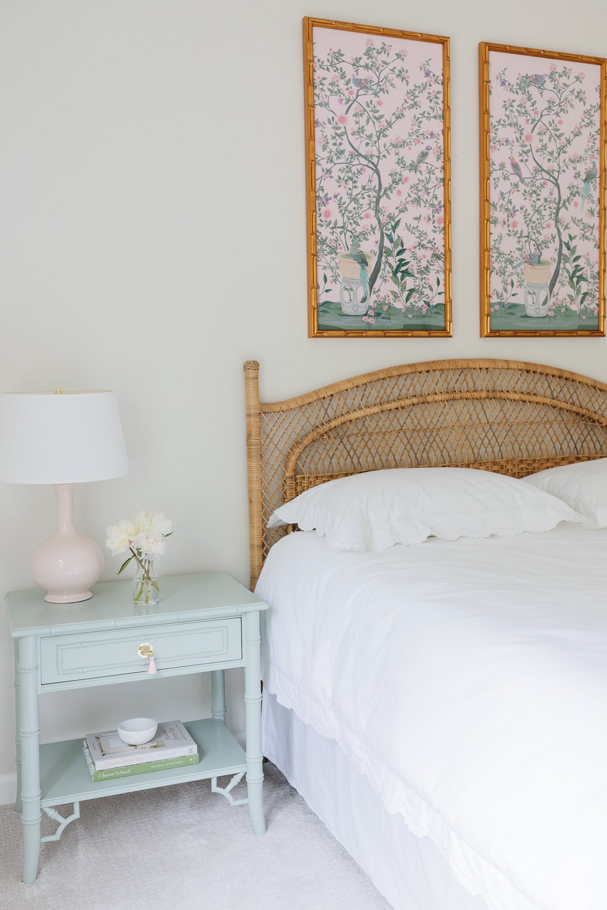 A guest bedroom with a rattan headboard and pink and green chinoiserie art above.