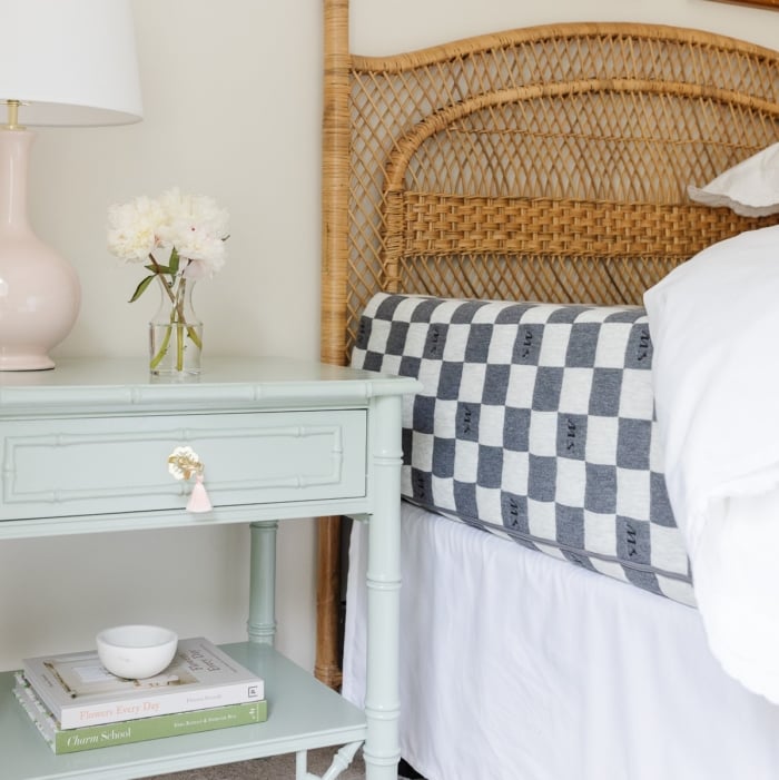 A guest bedroom with a rattan headboard and the bedding pulled back to show a guest room mattress.