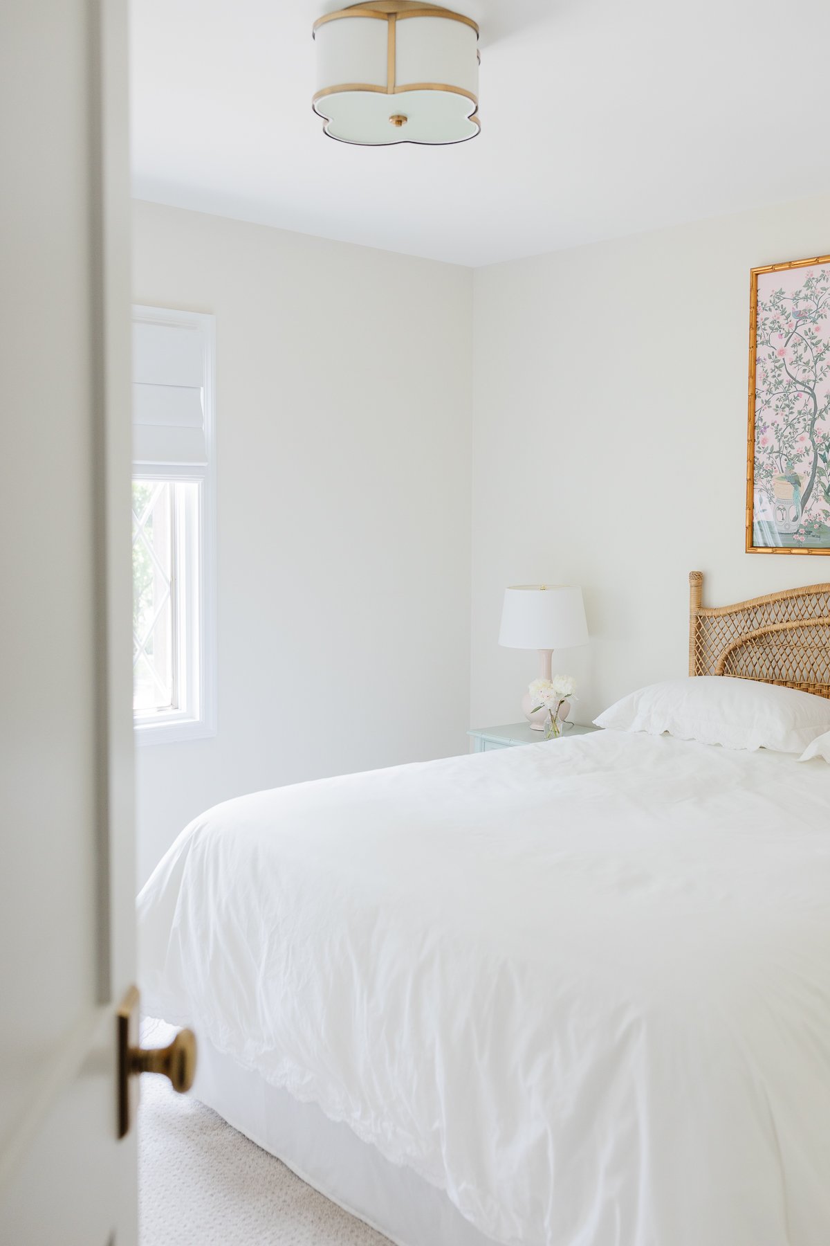 A guest bedroom with a rattan headboard and pink and green chinoiserie art above.