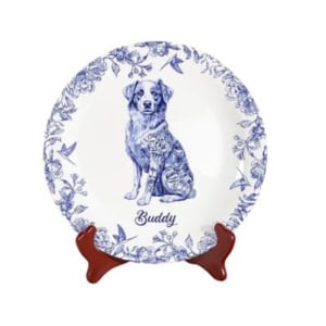 White ceramic plate with blue floral border, featuring an illustration of a dog in the center and the name "Buddy" below, displayed on a wooden stand—perfect for showcasing with plate hangers.
