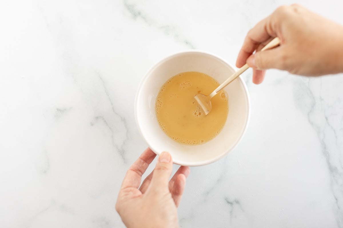 Overhead view of egg wash being whisked in small white bowl with fork