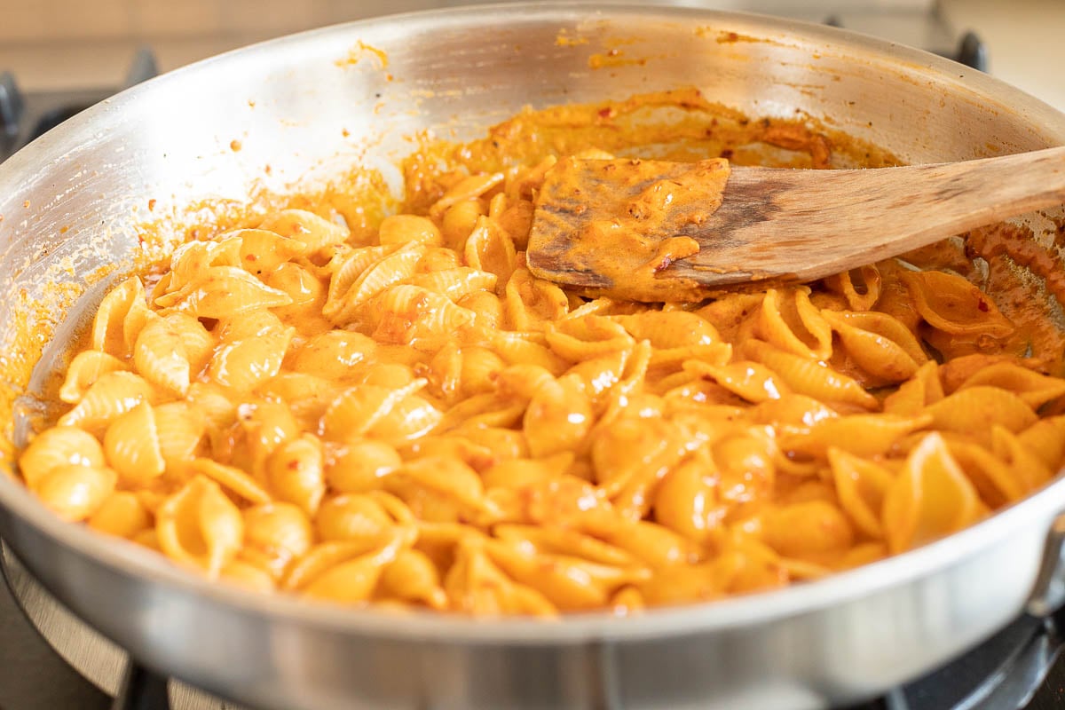 A stainless steel pan on a stovetop, filled with pasta. Image is part of a tutorial on how to reheat pasta.