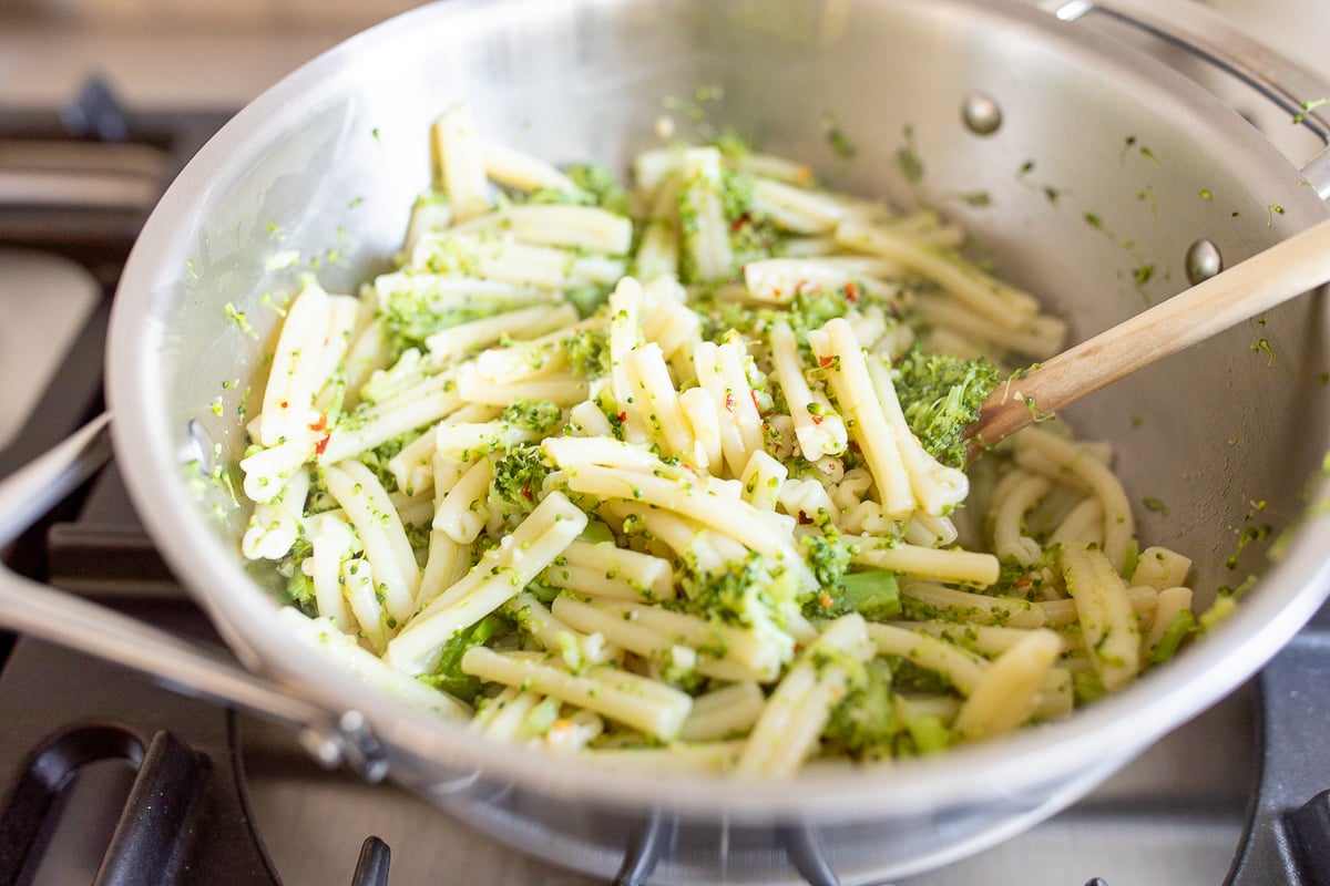 A stainless steel pan on a stovetop, filled with pasta. Image is part of a tutorial on how to reheat pasta.