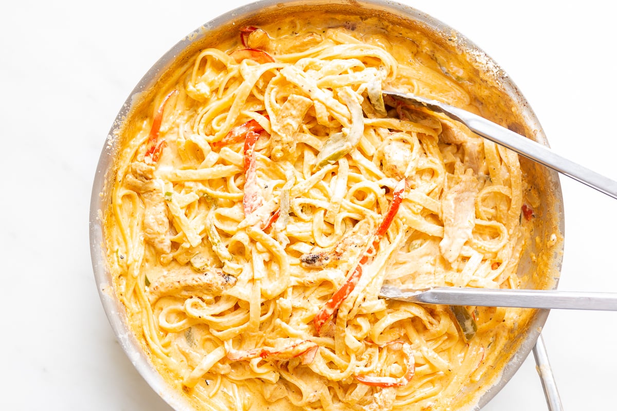 A stainless steel pan on a stovetop, filled with pasta. Image is part of a tutorial on how to reheat pasta.