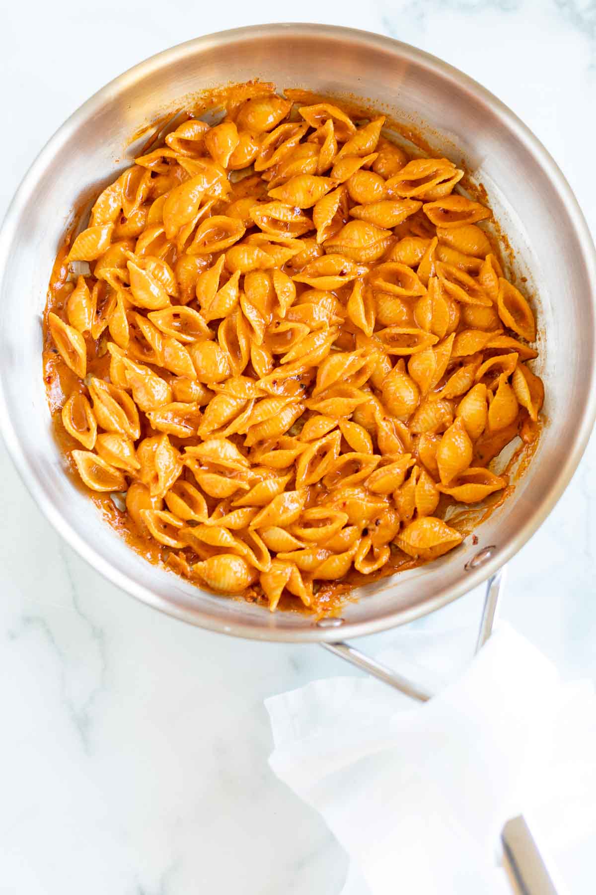 A stainless steel pan on a stovetop, filled with pasta. Image is part of a tutorial on how to reheat pasta. 