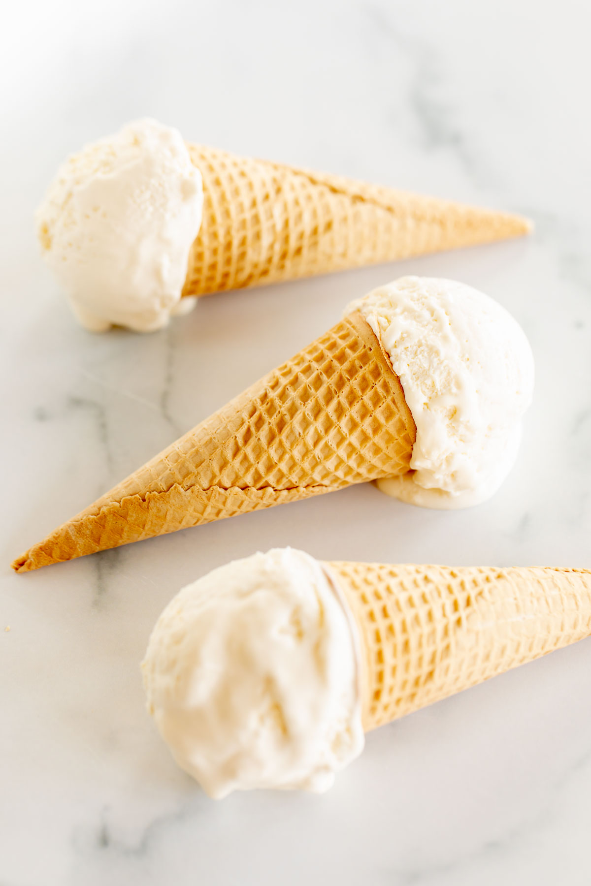 Three waffle cones filled with marshmallow ice cream on a marble countertop. 