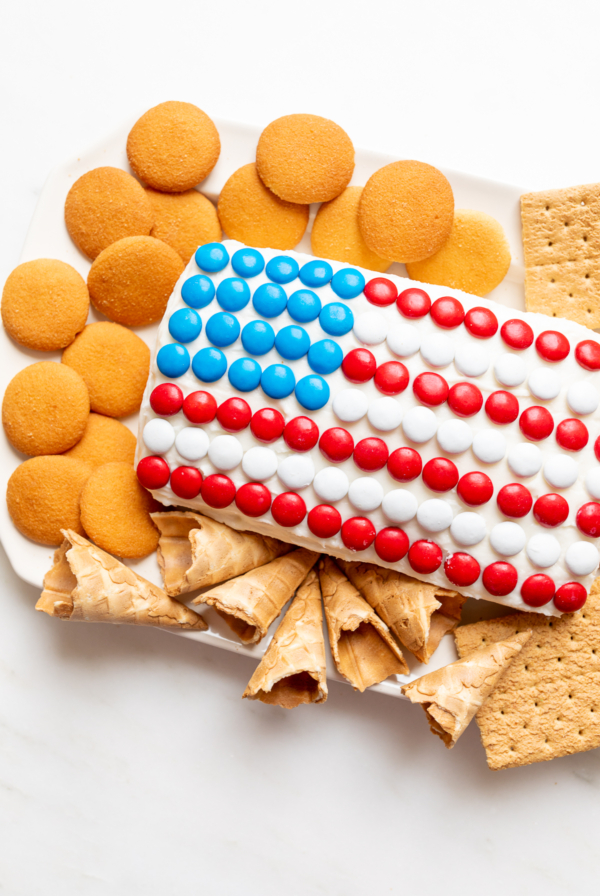 A red white and blue snack made of Funfetti dip in a flag shape, on a plate of cookies and crackers.