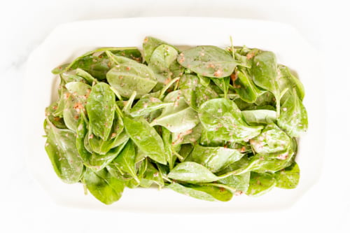 A white rectangular dish filled with fresh spinach leaves coated in a creamy dressing