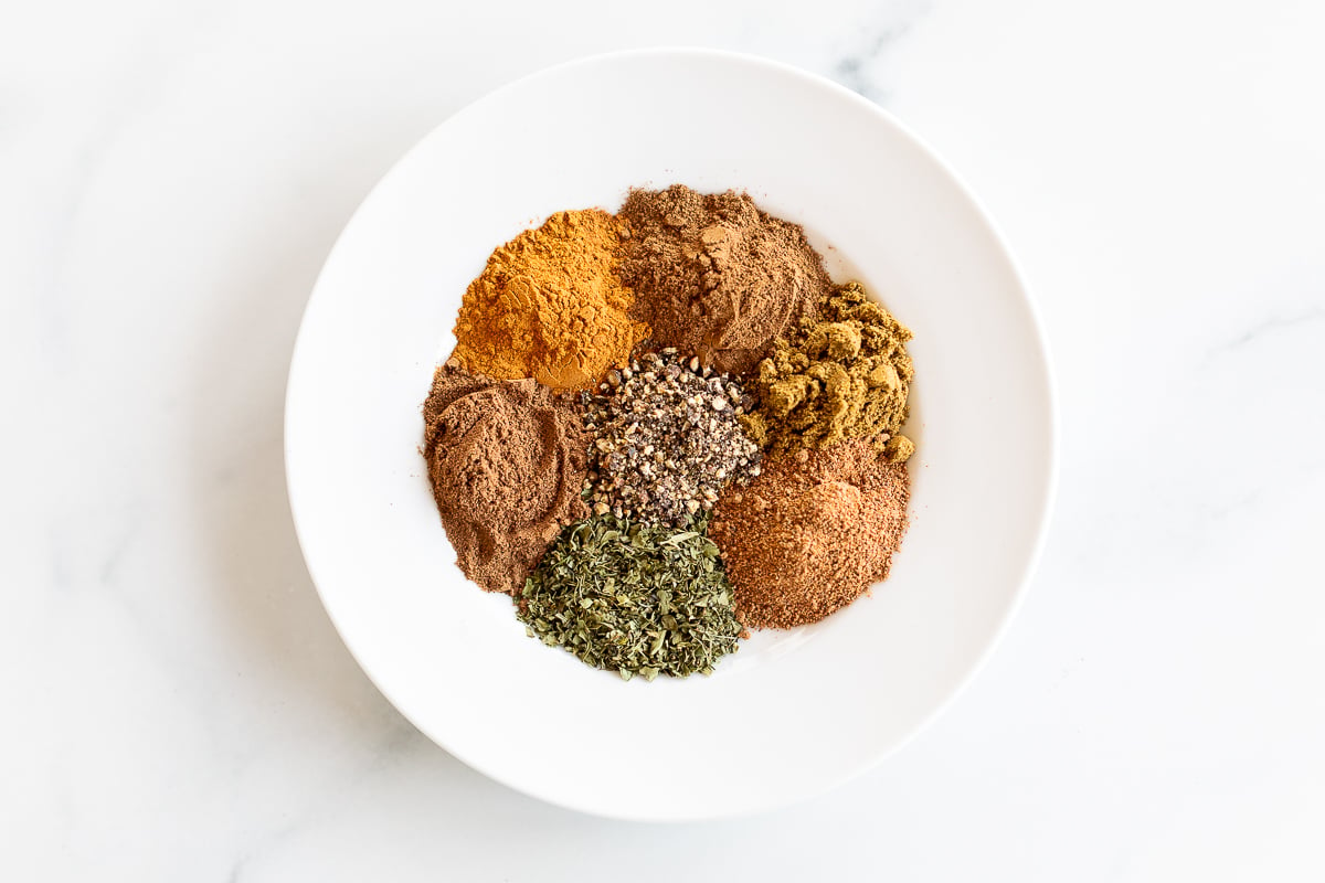 Overhead view of ingredients for seven spice in white bowl