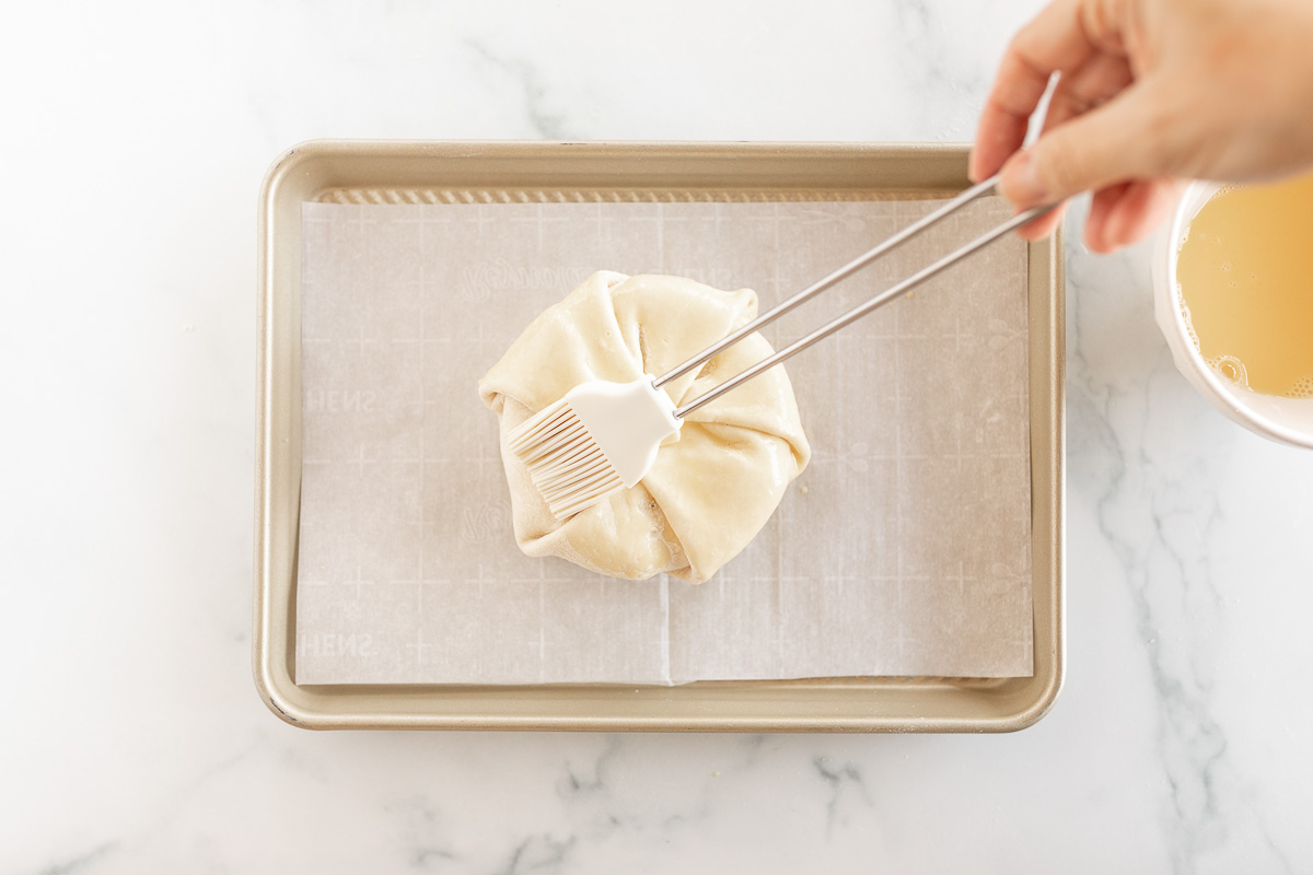 Hand using silicone brush to brush eggwash onto pastry-wrapped brie