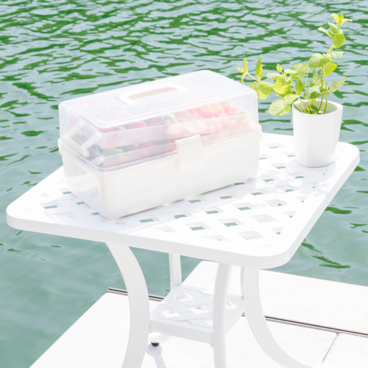 A tackle box charcuterie display on a white table with water in the background.