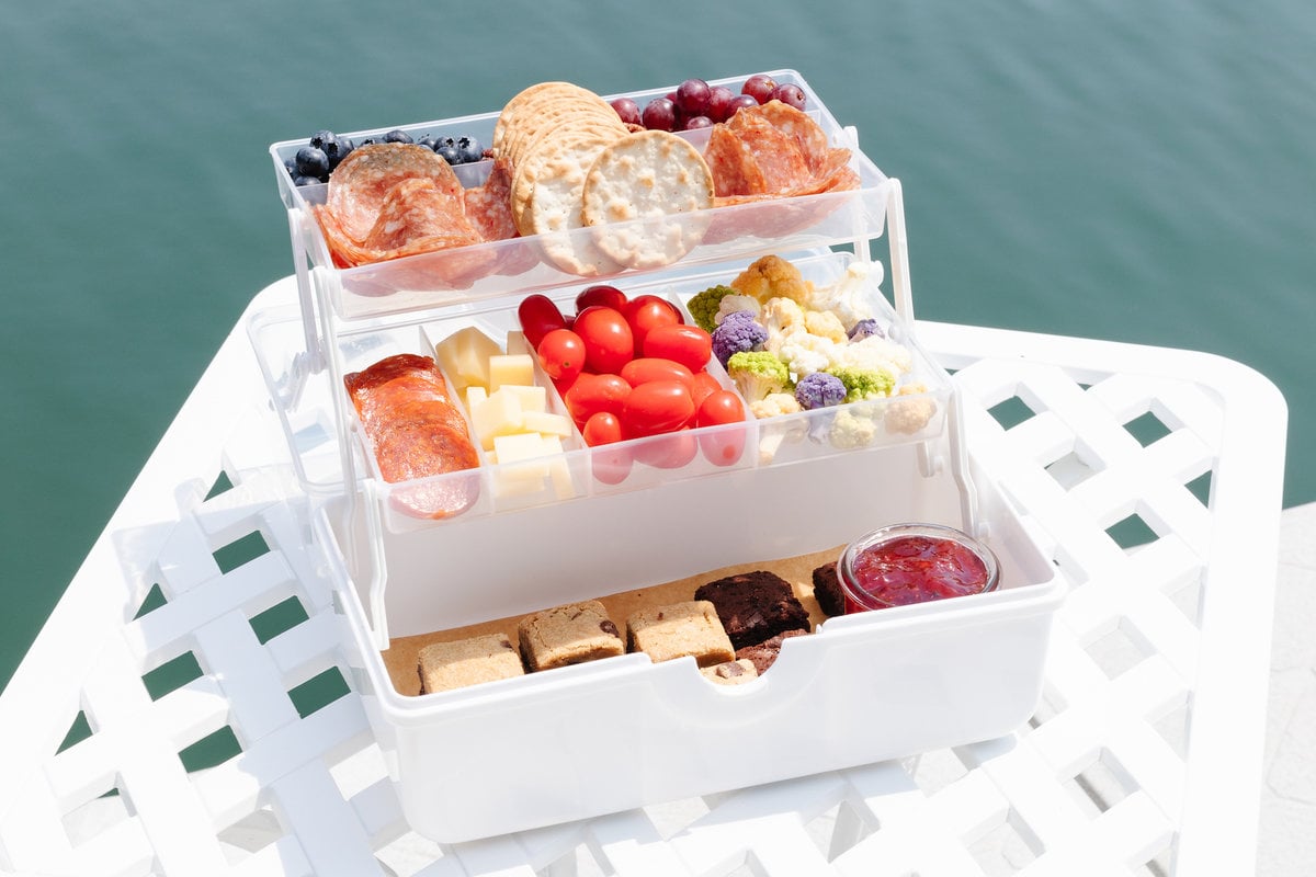 A tackle box charcuterie display on a white table with water in the background.