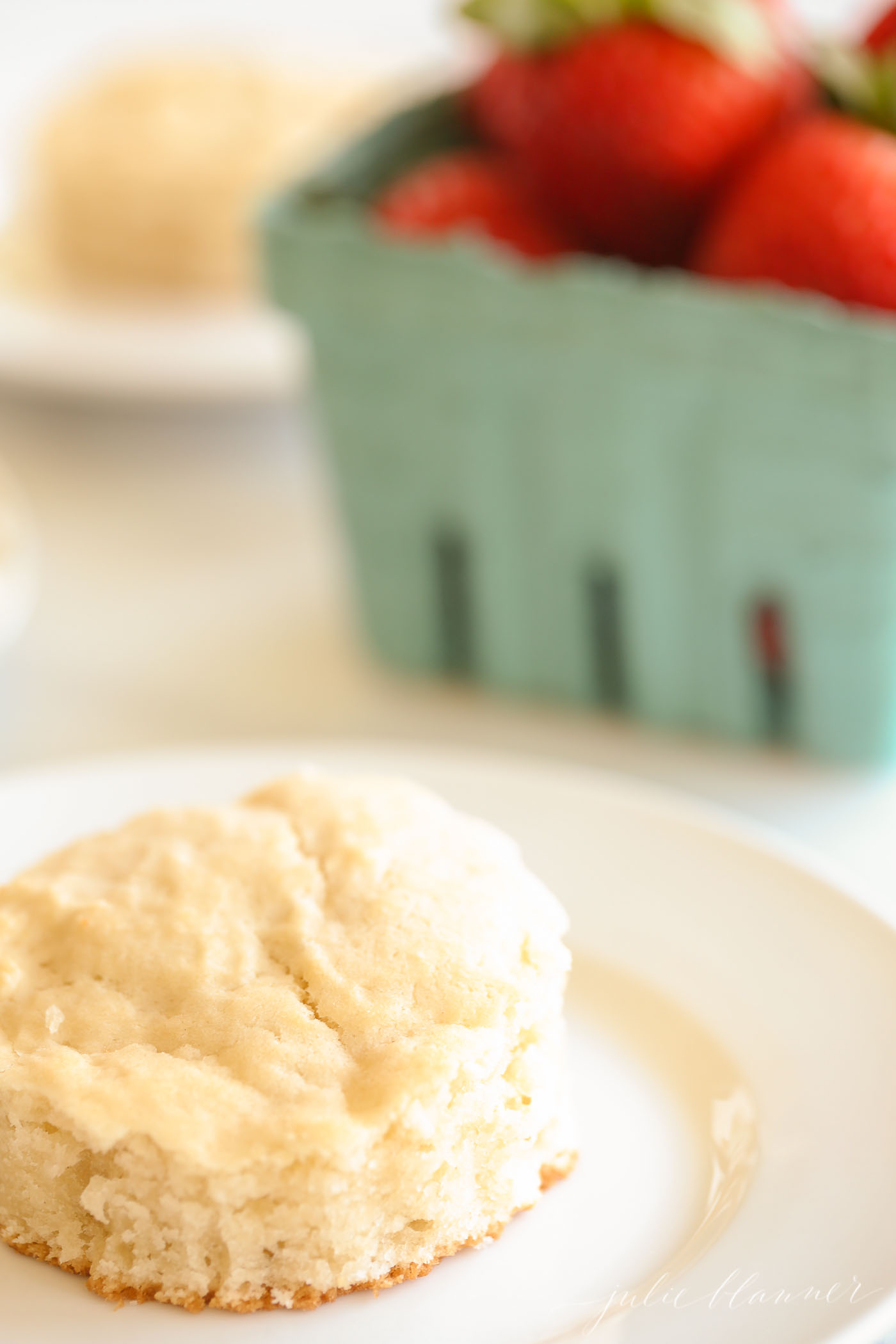 A biscuit and a box of strawberries in the background for a strawberry shortcake recipe.