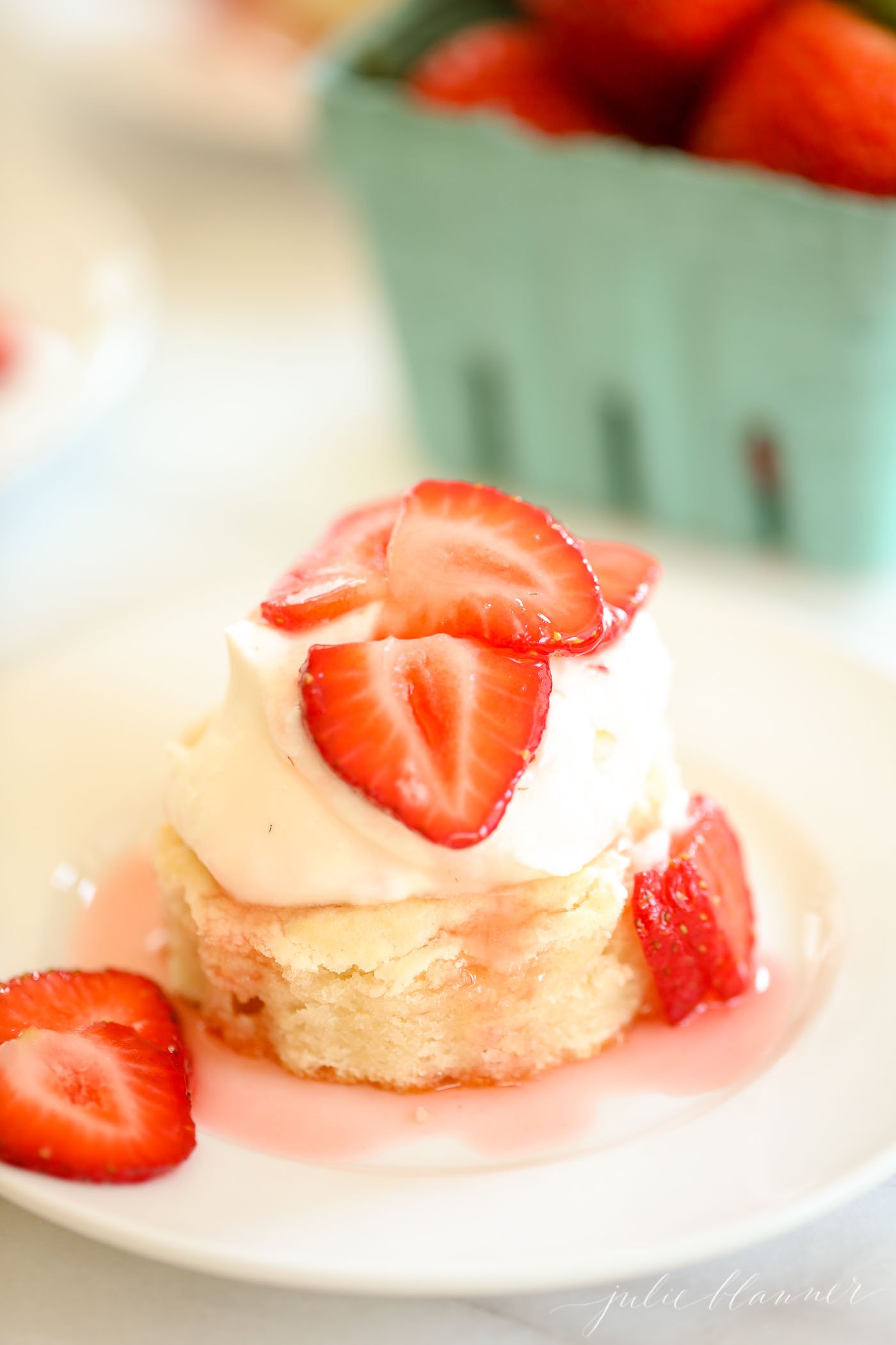 strawberry shortcake on a white plate, blue box of strawberries in background.