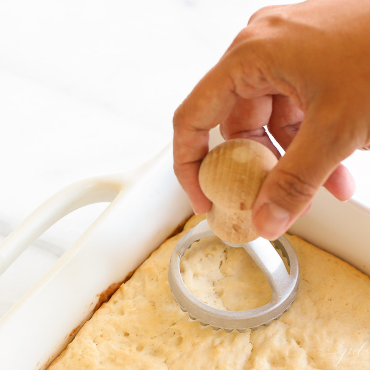 A hand cutting into a white pan full of shortcake with a round cutter.
