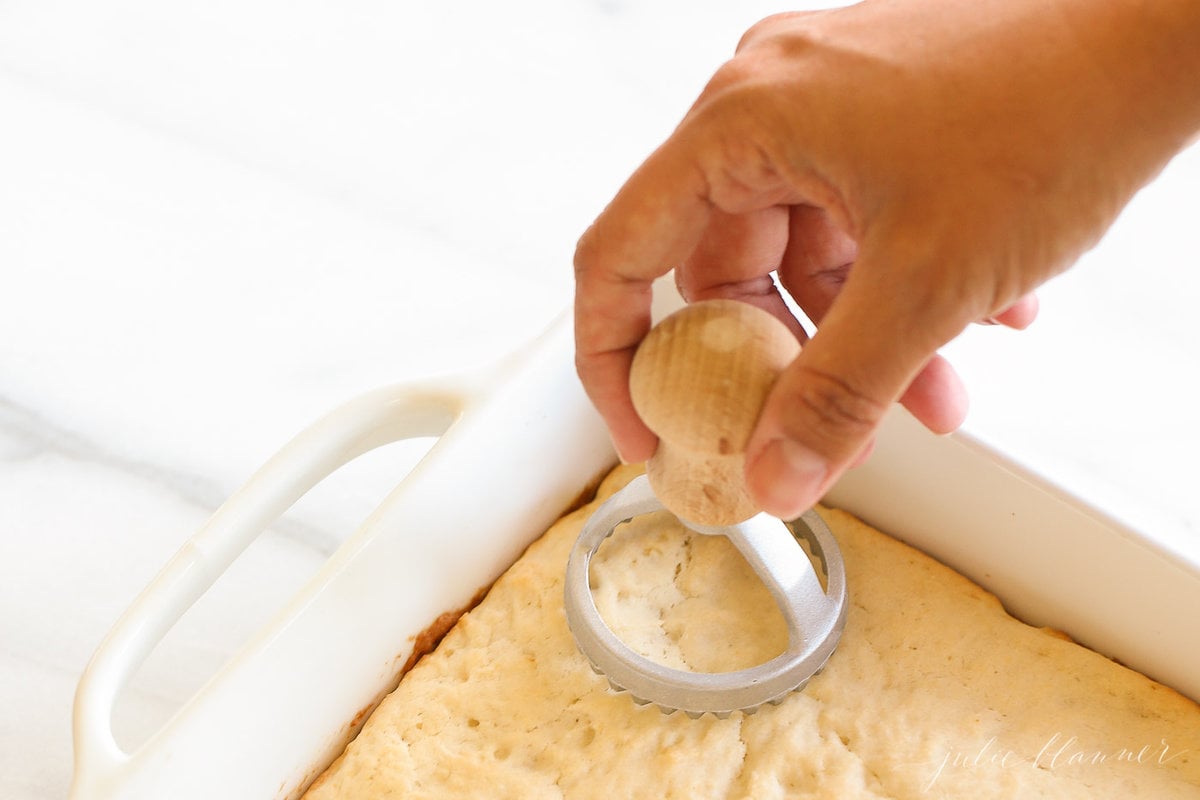 A hand cutting into a white pan full of shortcake with a round cutter.