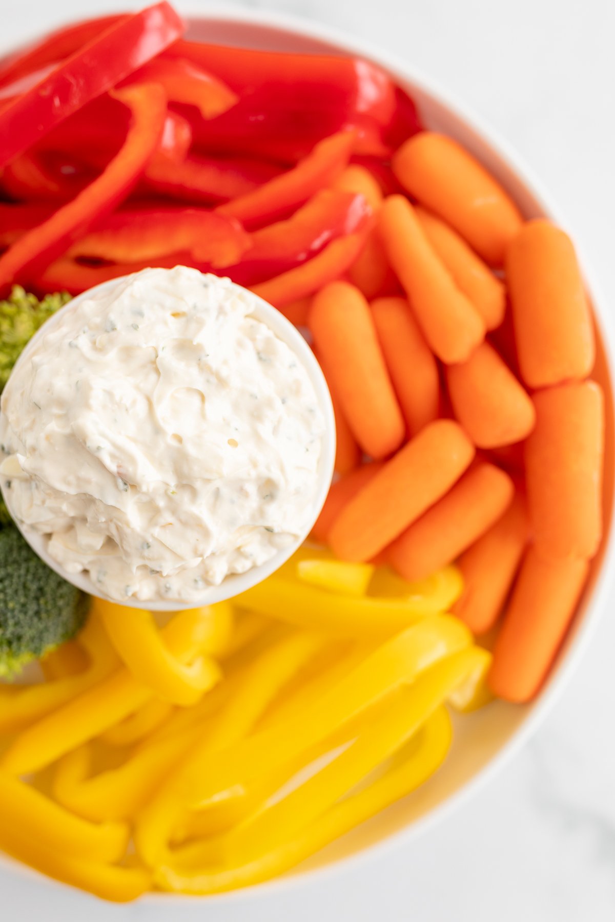 A bowl of veggie dips surrounded by sliced peppers and baby carrots. 