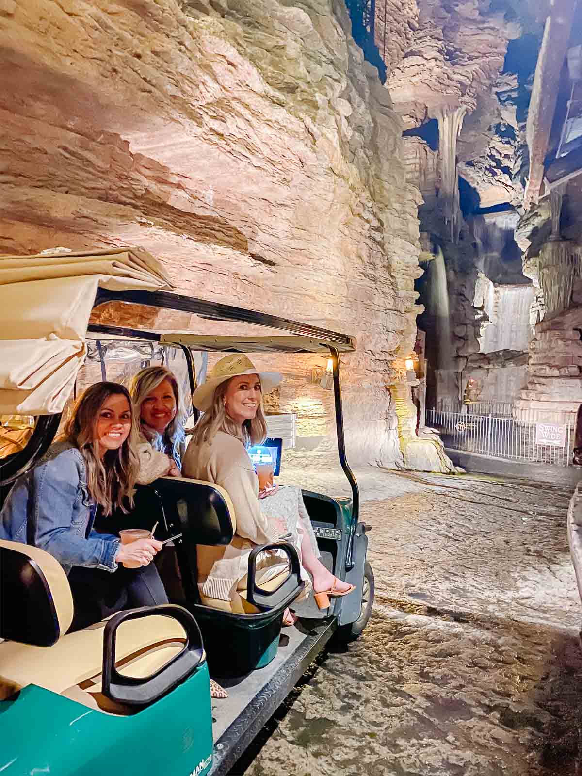 Three people sitting in a golf cart inside a cave with stalactites and rock formations in the background, showcasing one of the unique things to do in Branson.
