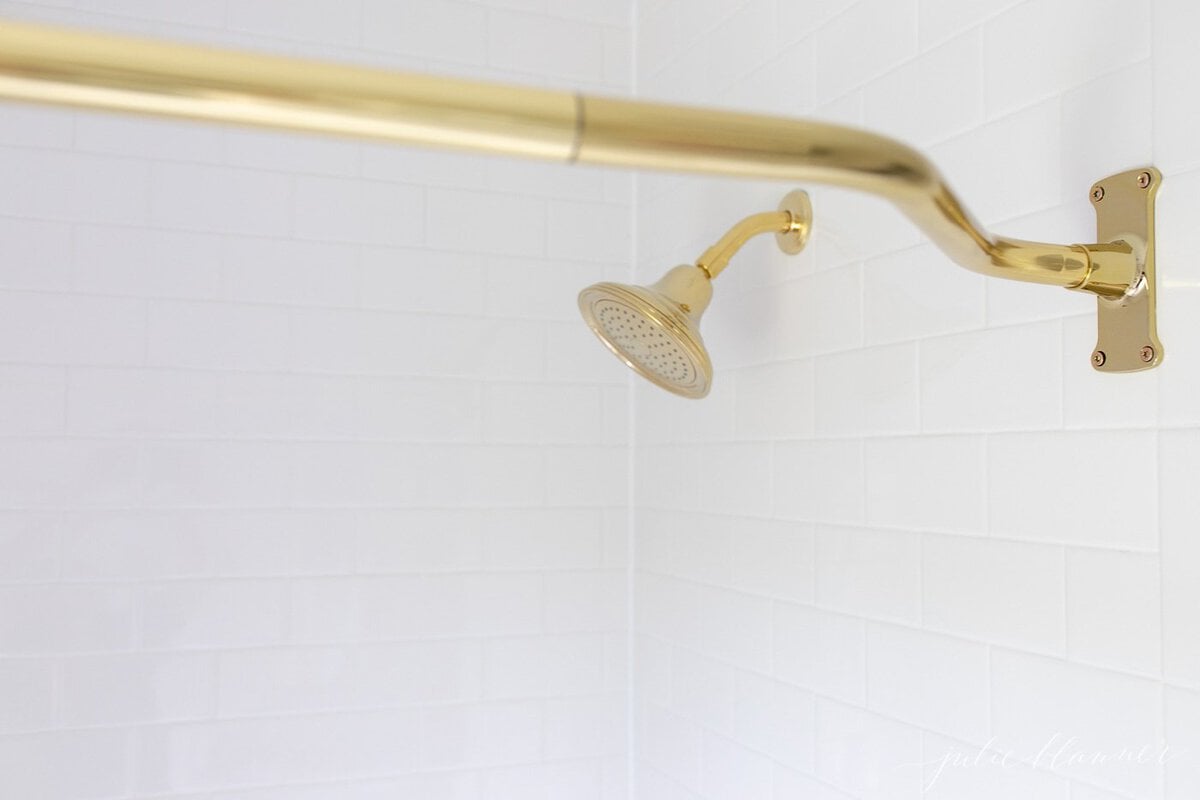 A white tiled shower with a curved brass shower curtain rod.