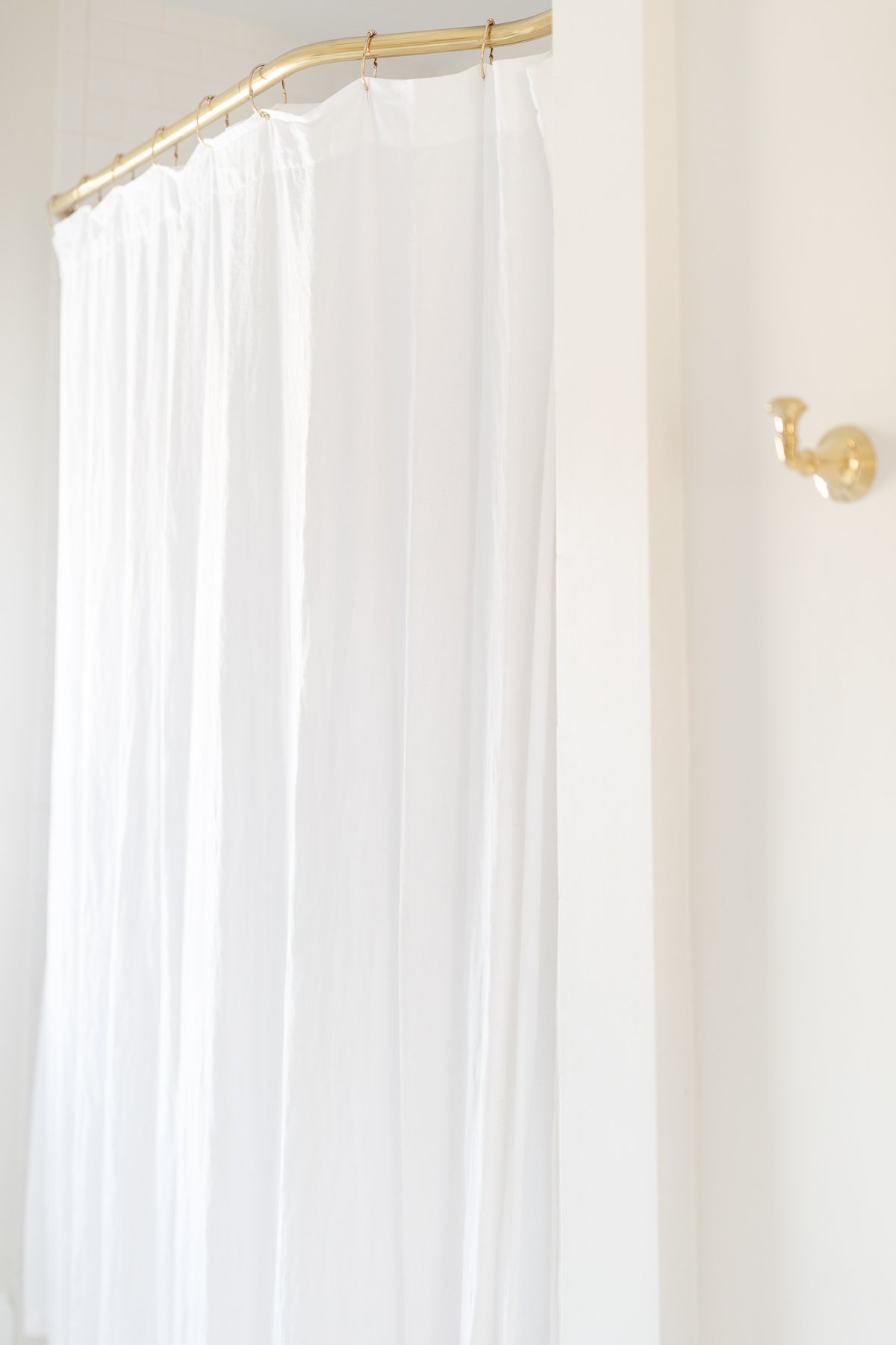 A white shower with a brass shower curtain rod.
