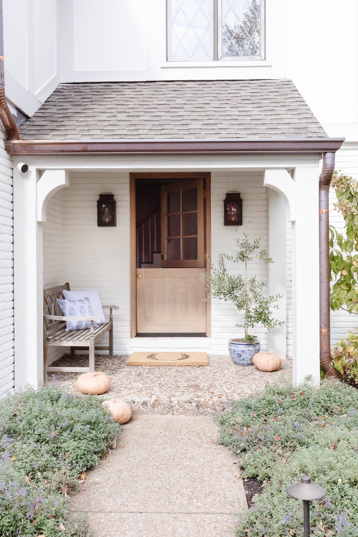netural brick house with dutch door copper lanterns and porch decorated for fall
