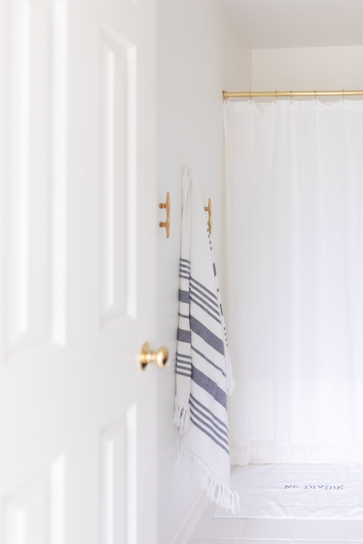 A white bathroom with a gold shower curtain rod with a white tasseled curtain.