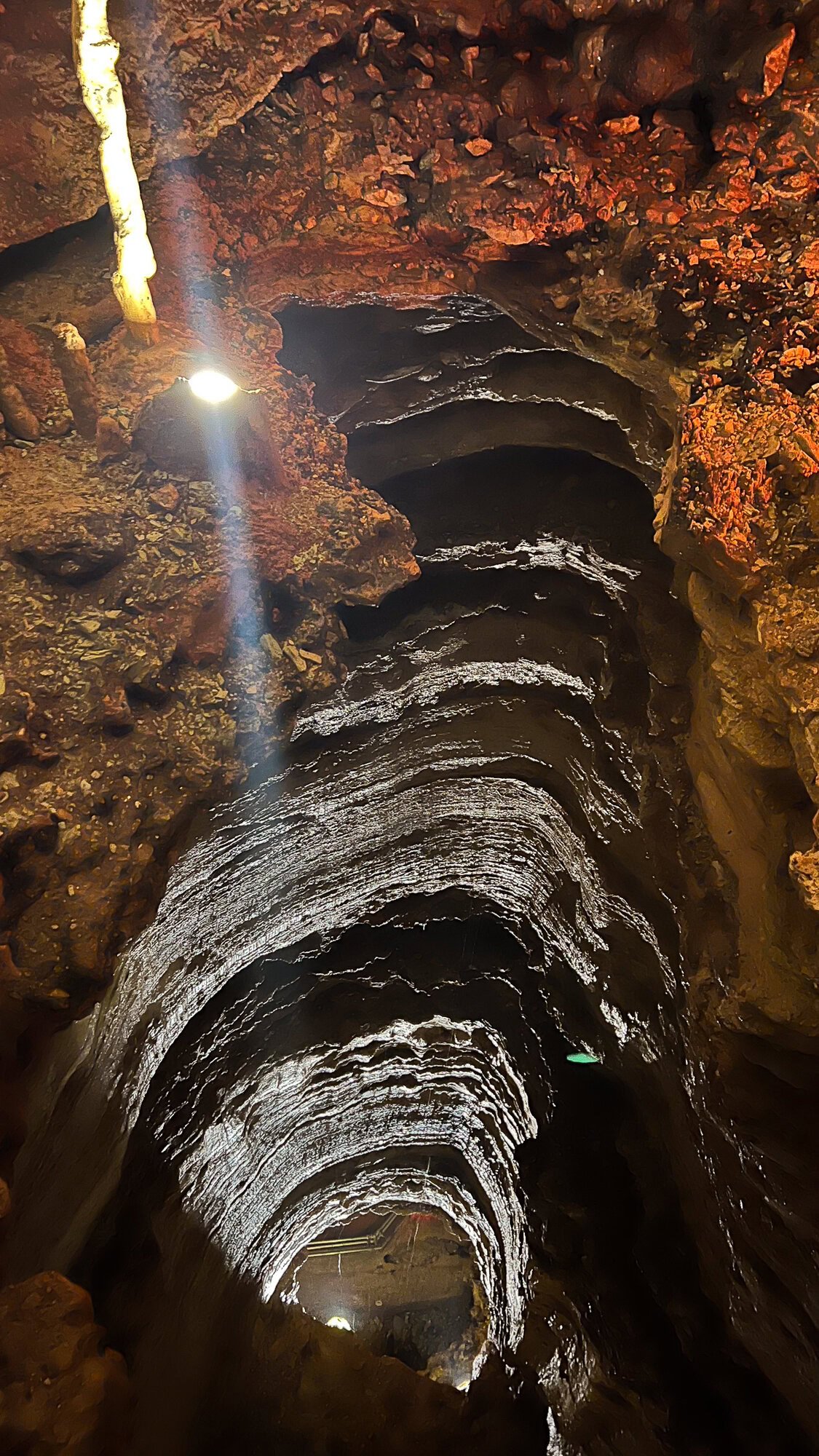 A deep vertical cave with layered rock walls, illuminated by artificial lights highlighting the textures and depth of the shaft—a hidden gem among things to do in Branson.