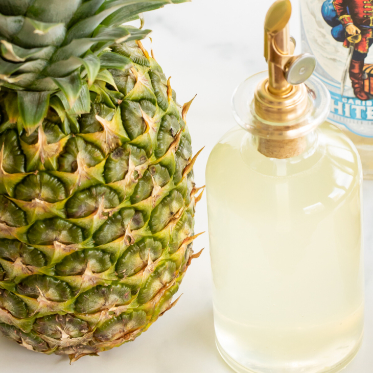 Bottle of pineapple simple syrup set next to fresh pineapple and bottle of white rum
