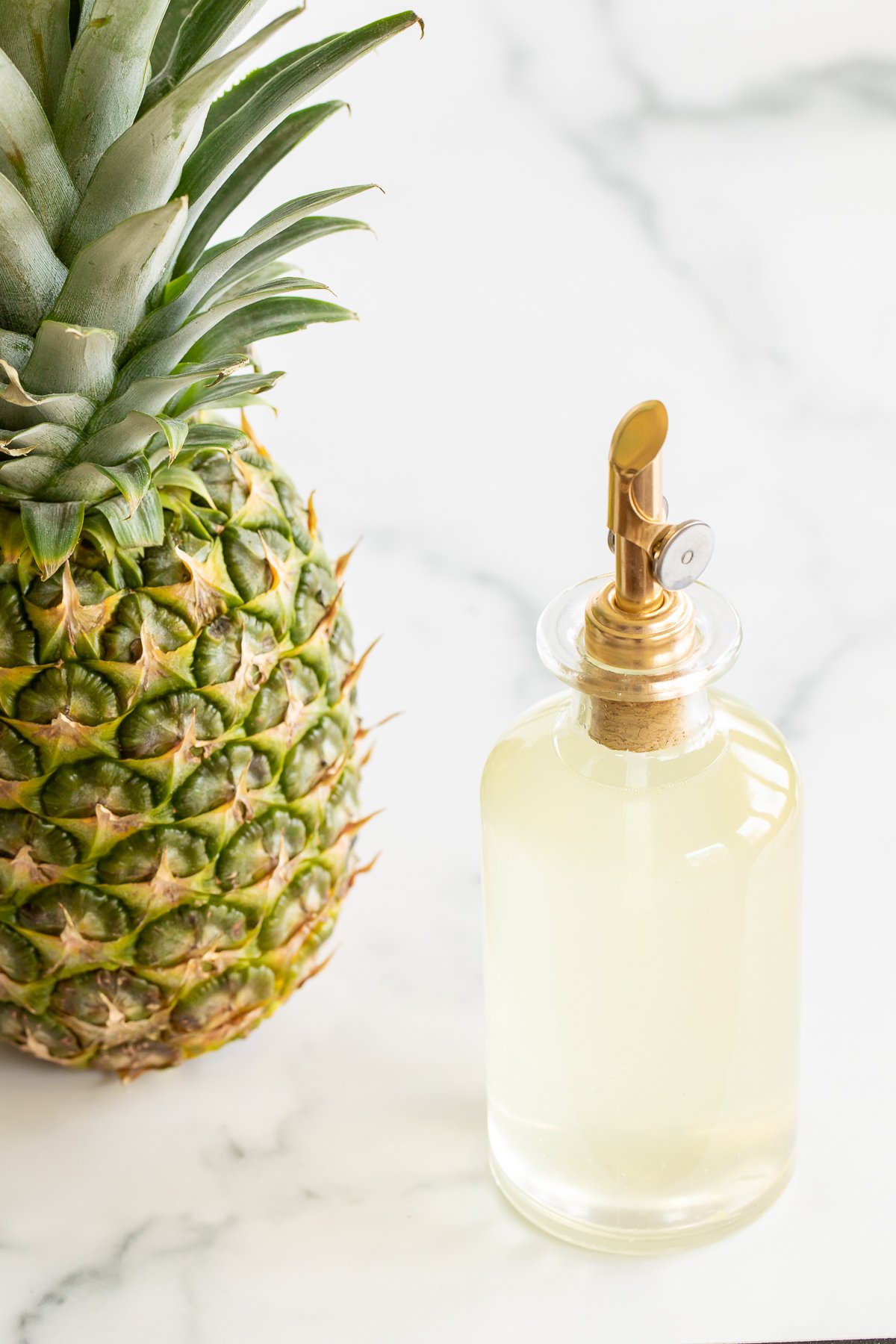 Bottle of pineapple simple syrup set next to fresh pineapple