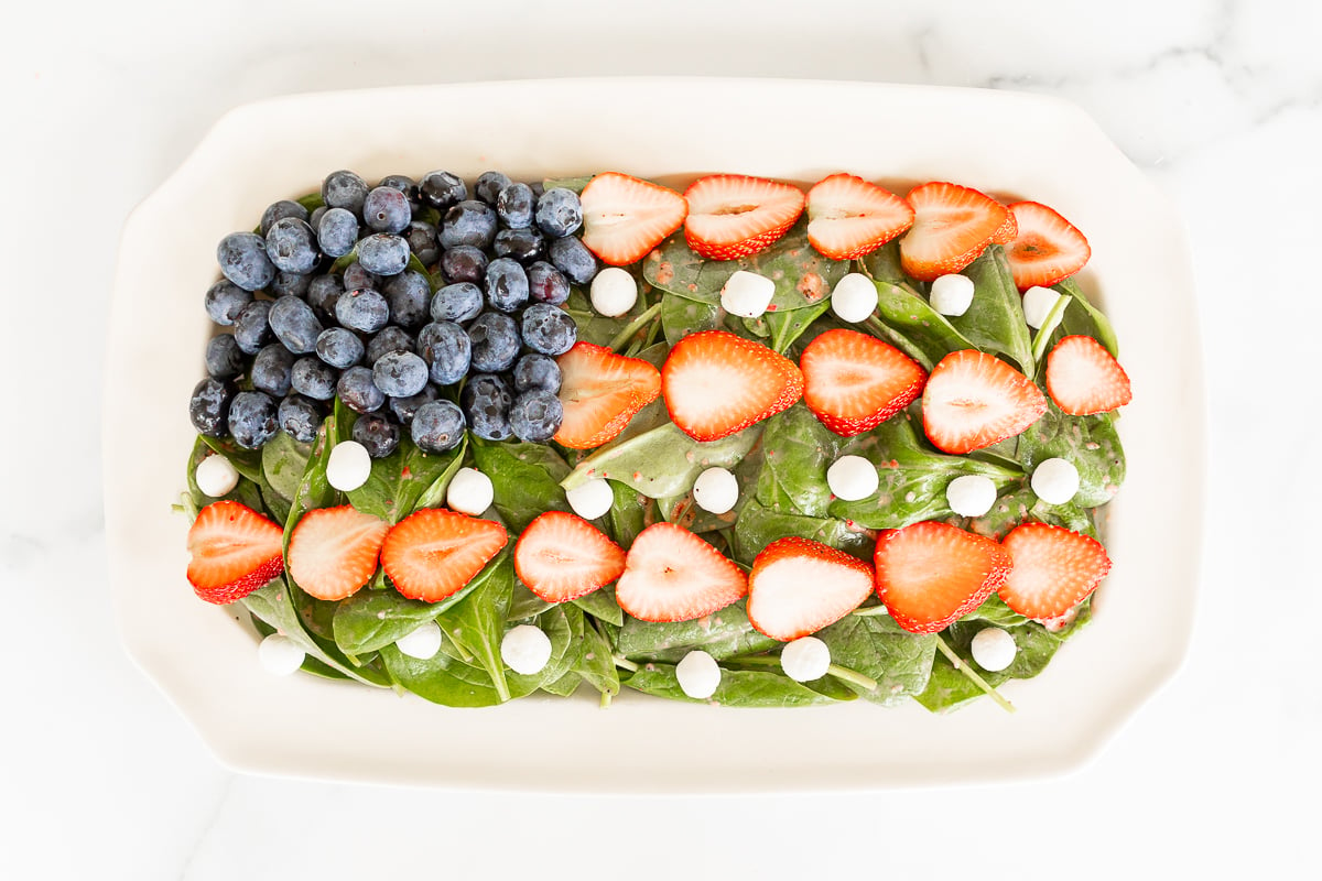 A red white and blue salad shaped into an American flag, on a white platter.