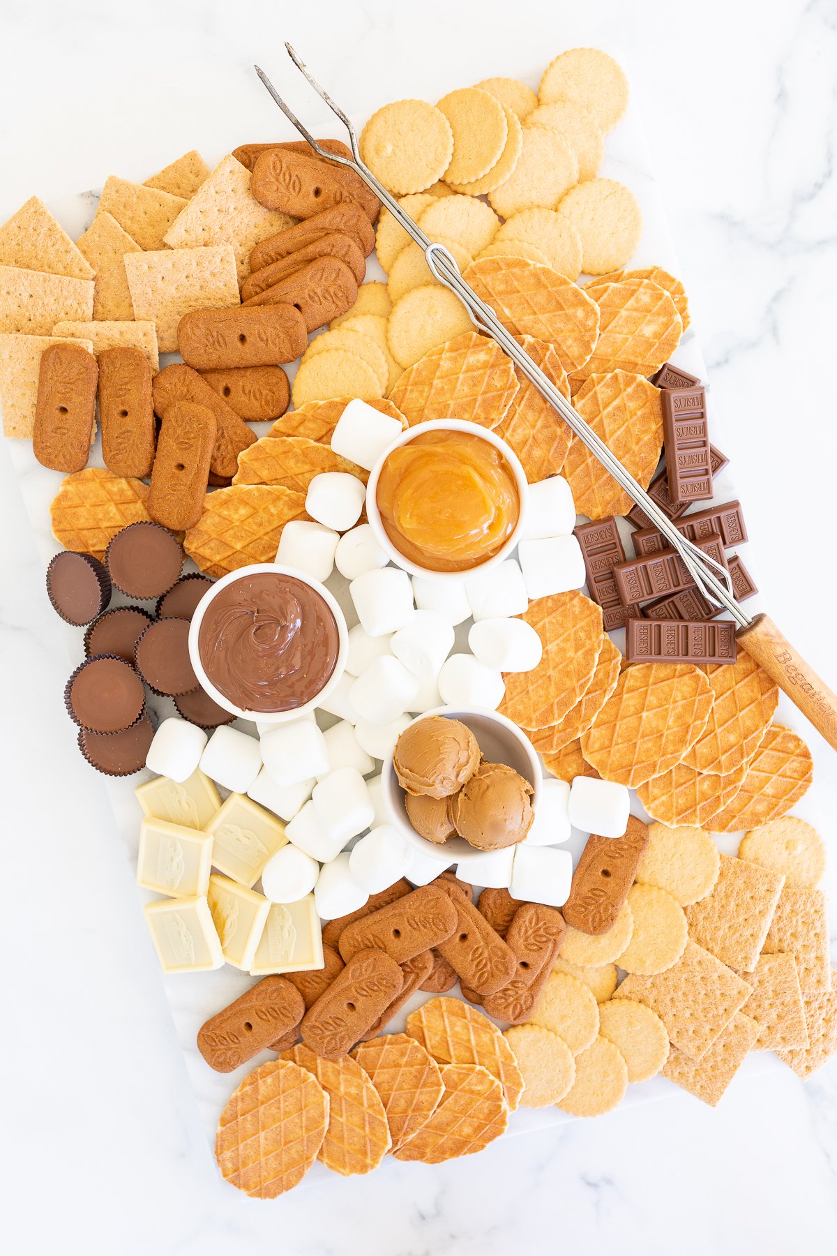 A s'mores charcuterie board filled with various marshmallows, cookies, crackers and dessert spreads.