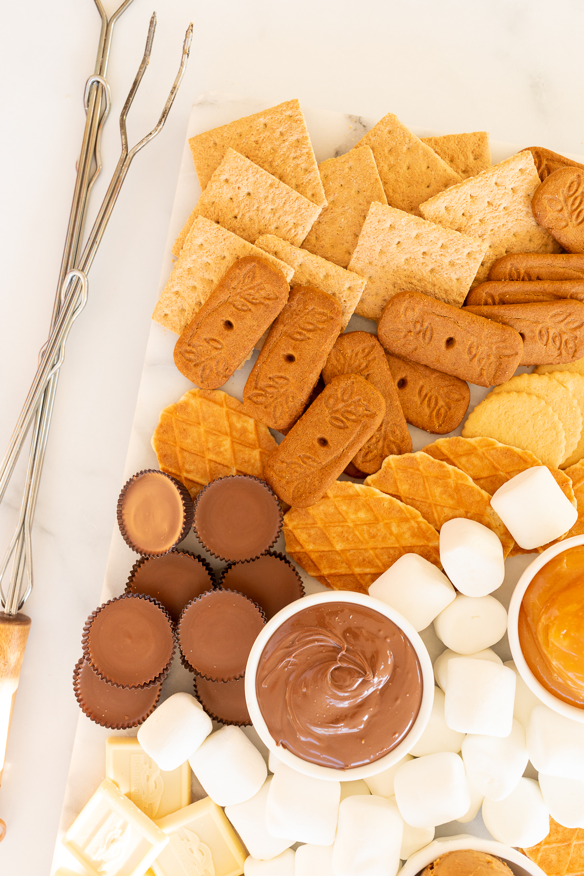 A s'mores board filled with various marshmallows, cookies, crackers and dessert spreads.