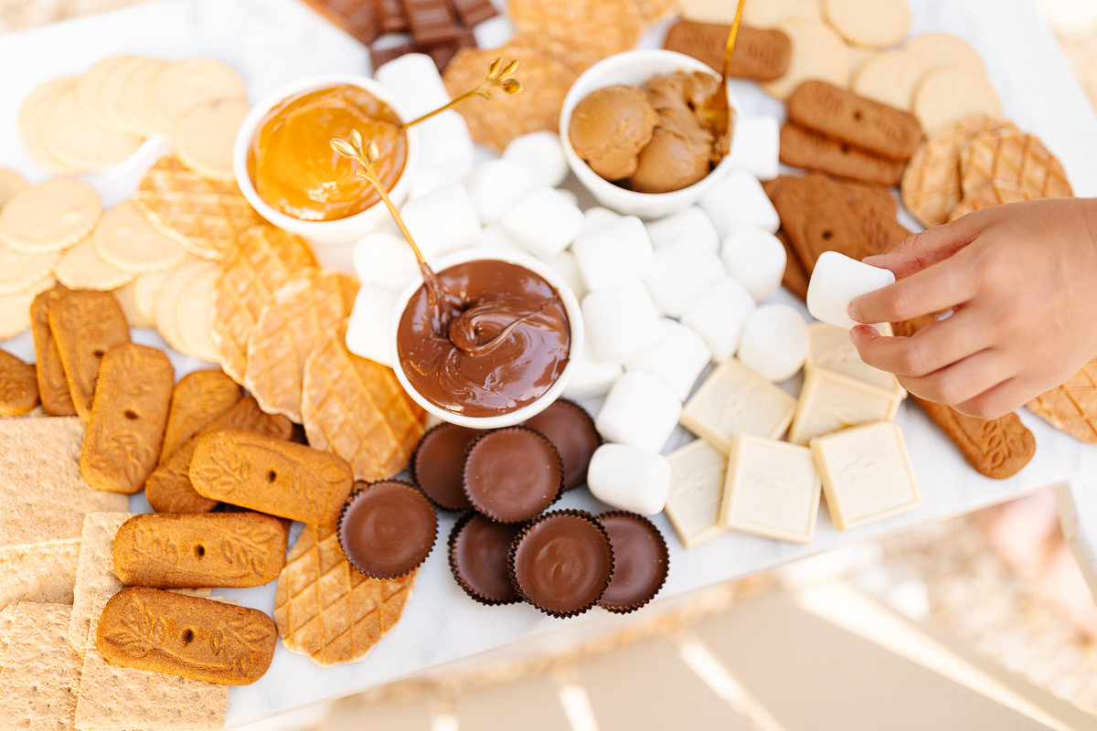 A smores charcuterie board filled with various marshmallows, cookies, crackers and dessert spreads.