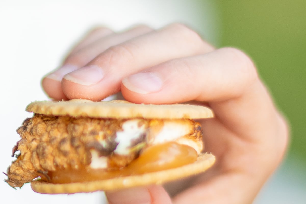 A hand holding a s'mores with caramel