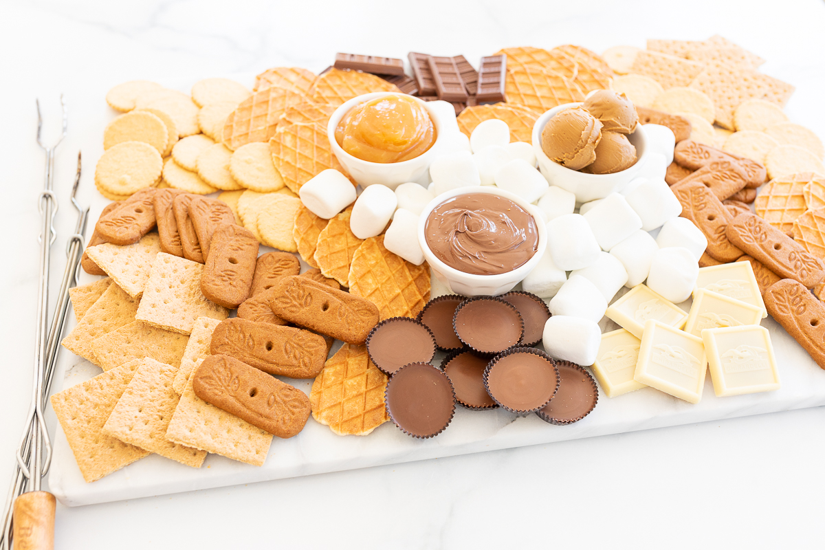 A s'mores board filled with various marshmallows, cookies, crackers and dessert spreads.