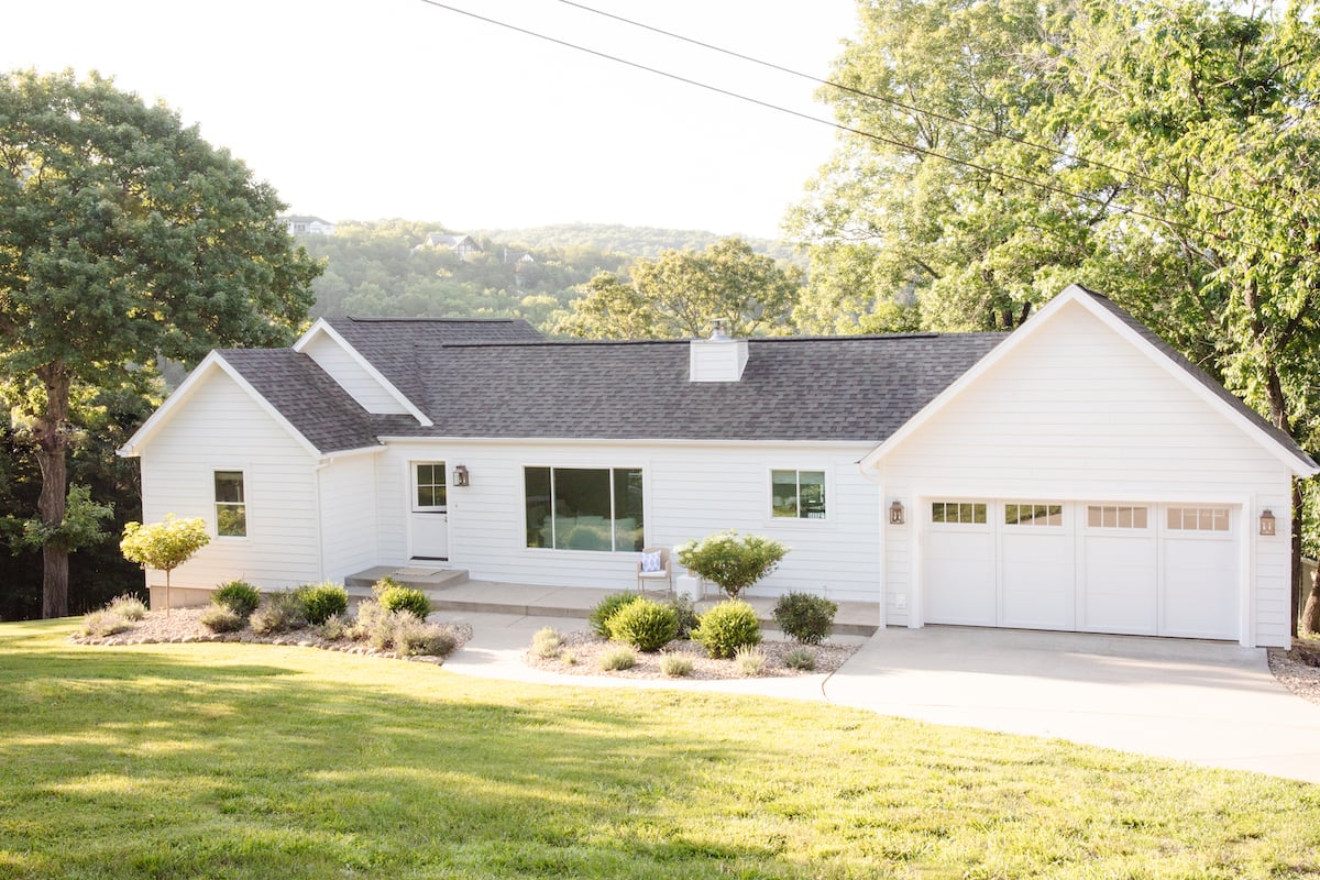 A white house with a gray roof and carriage garage doors.