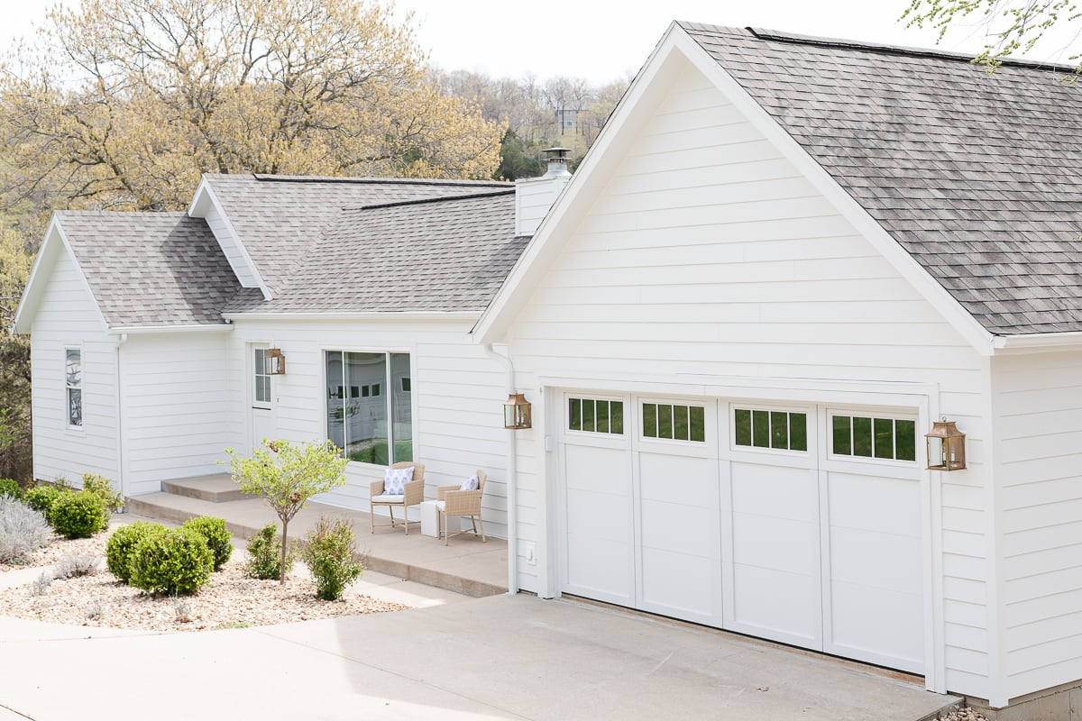 A white house with a gray roof and carriage garage doors.
