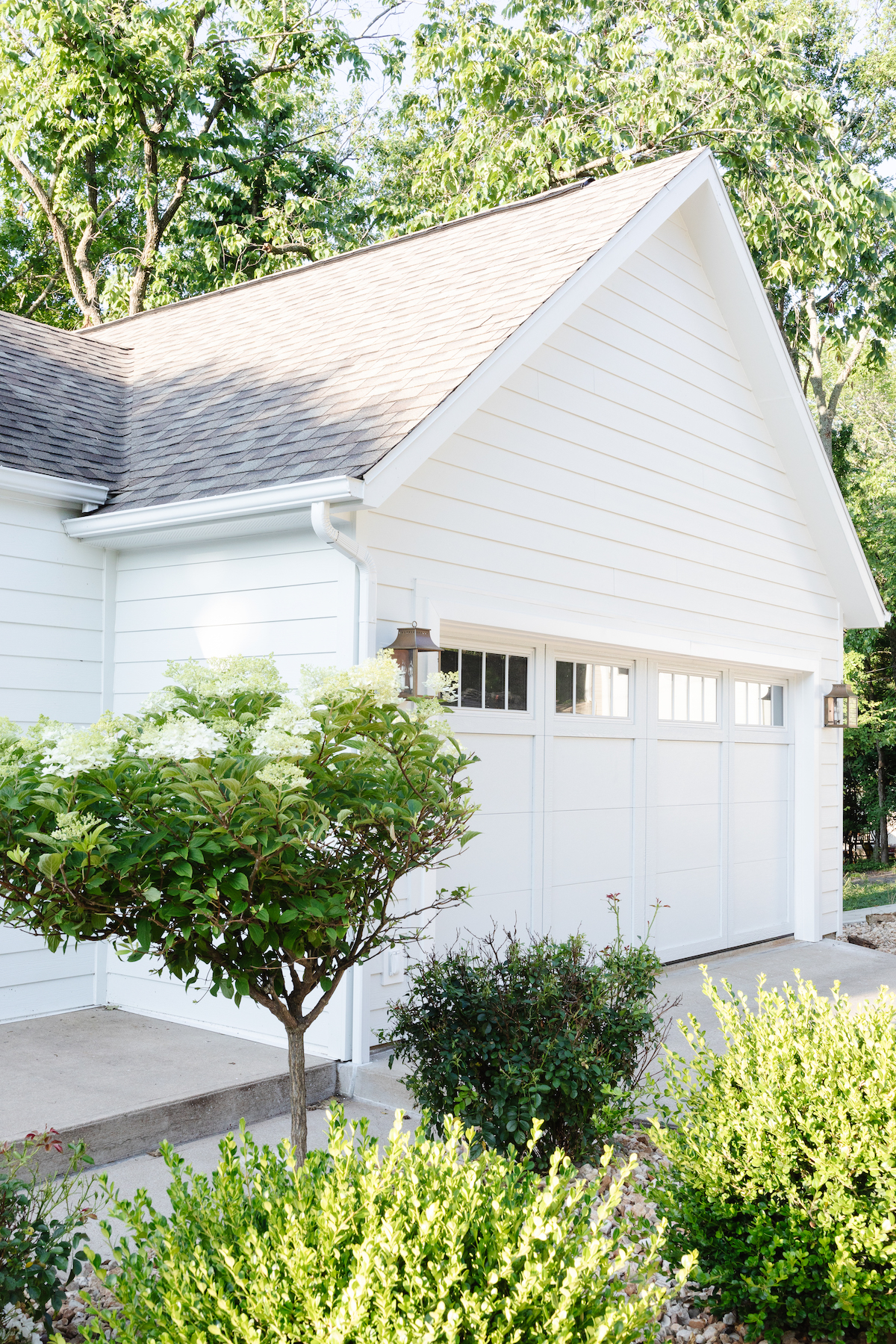 A white house with a gray roof and carriage garage doors.