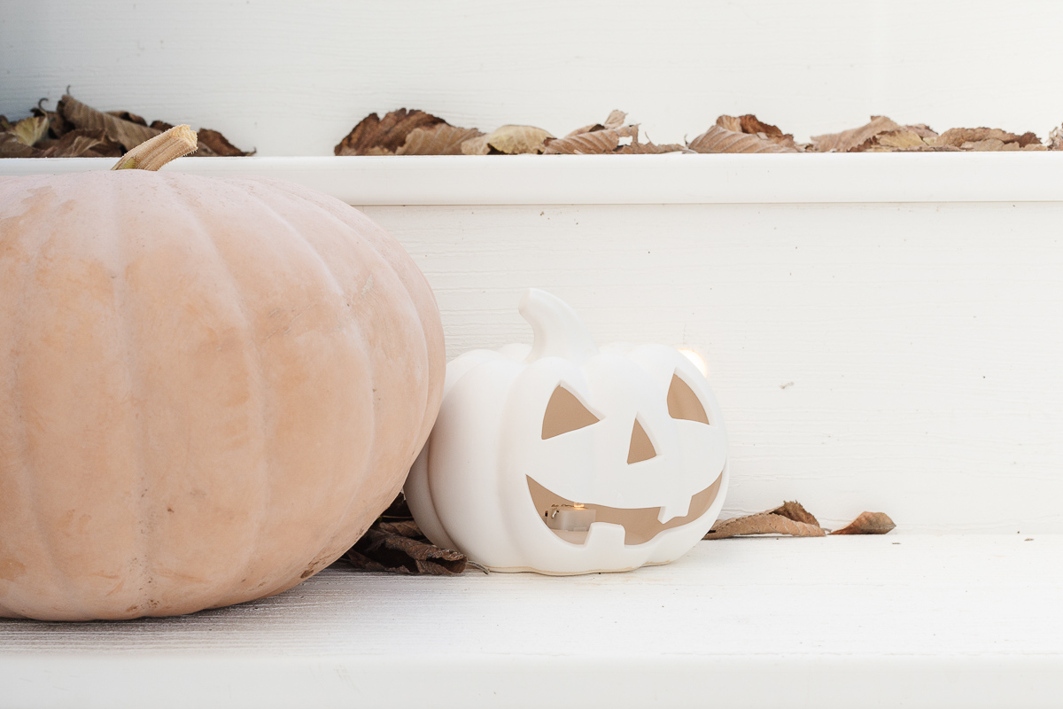 A white faux pumpkin jack o lantern and a peach faux pumpkin on white porch steps.