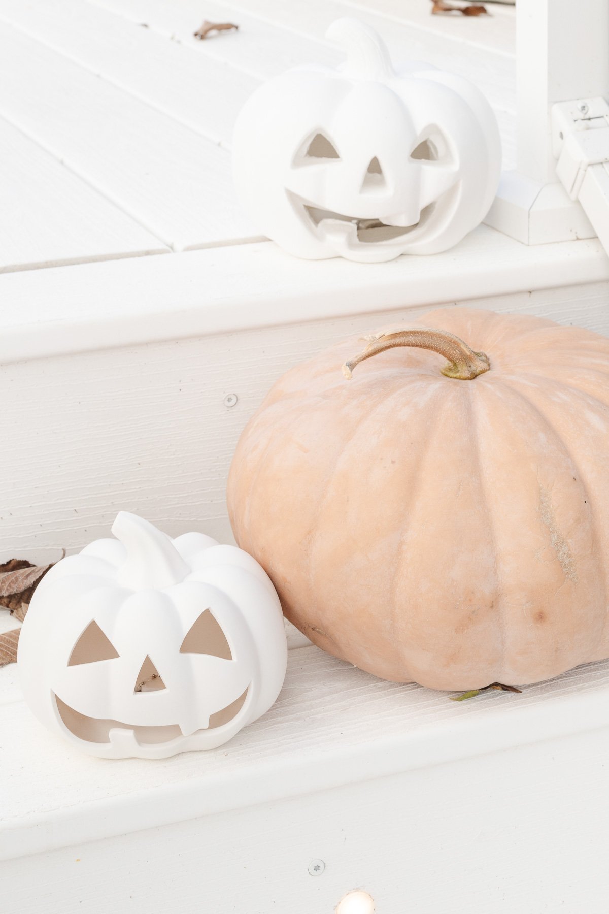 A white faux pumpkin jack o lantern and a peach faux pumpkin on white porch steps.